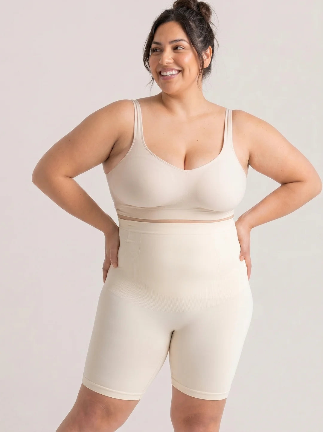 Chica sonriendo con los brazos en la cintura luce los shorts moldeadores invisibles de cintura alta sin costuras Shaperbodys de color beige